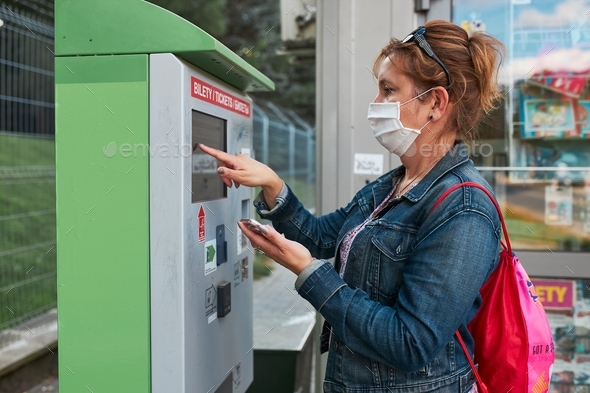 Woman buying bus ticket in ticket machine wearing face mask to cover mouth and nose
