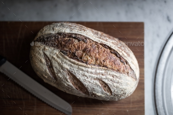 Rustic organic bread loaf on timber cutting board in kitchen lit by natural light