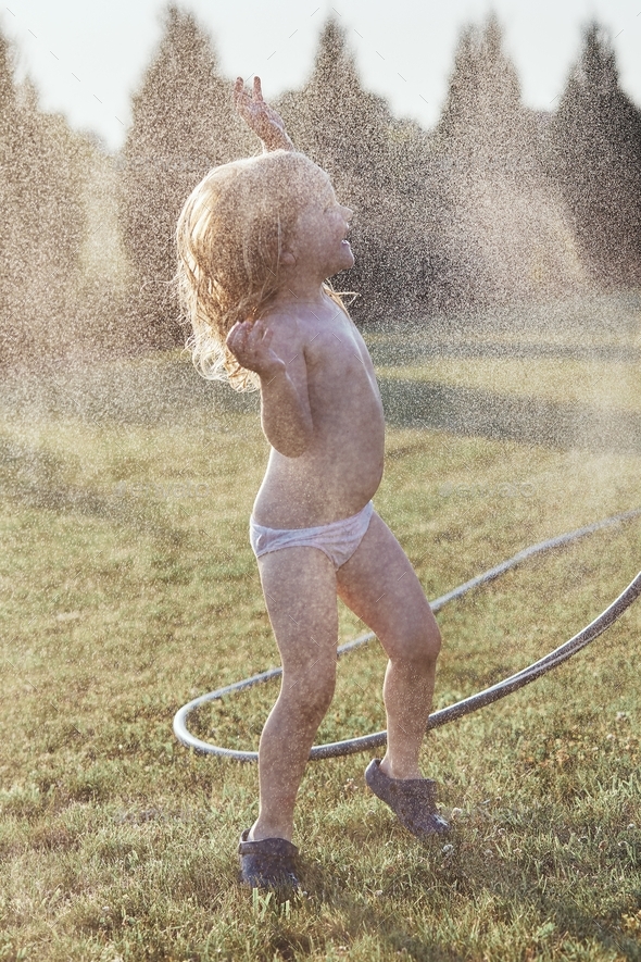 Little cute adorable girl enjoying a cool water sprayed by her