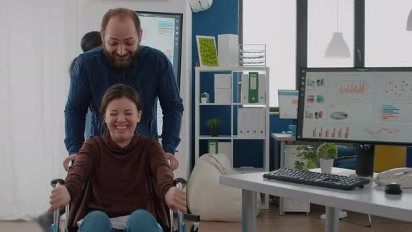 Man Employee Taking Break Pushing Wheelchair with His Paralysed Colleague alt