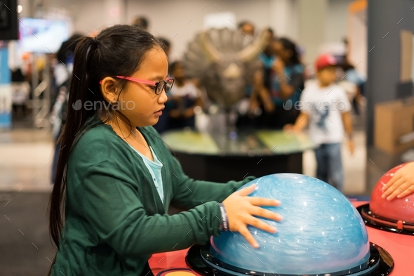 young girl wearing glasses is holding a semi sphere science interactive item