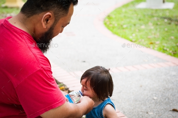 father gives toddler daughter drinks from water bottle in the park
