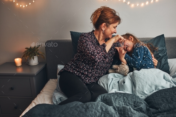 Mother playing with her little daughter in bed, having fun before going sleep. Mom tickling child