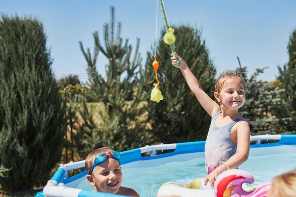Children playing in a pool with fishing rod toy in a home garden. Kids  having fun playing together Stock Photo by przemekklos