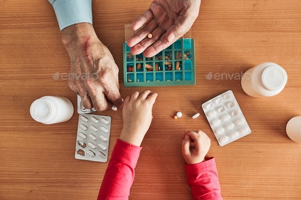 Grandchild helping grandfather to organize medication into pill dispenser. Senior man taking pills