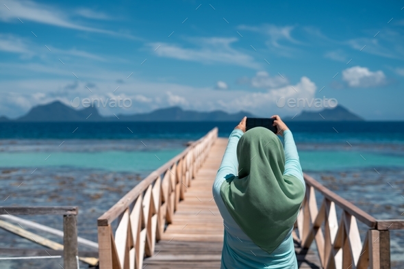 Hijab woman taking photo of the scenery using mobile phone. Beautiful sea in Semporna, Sabah.