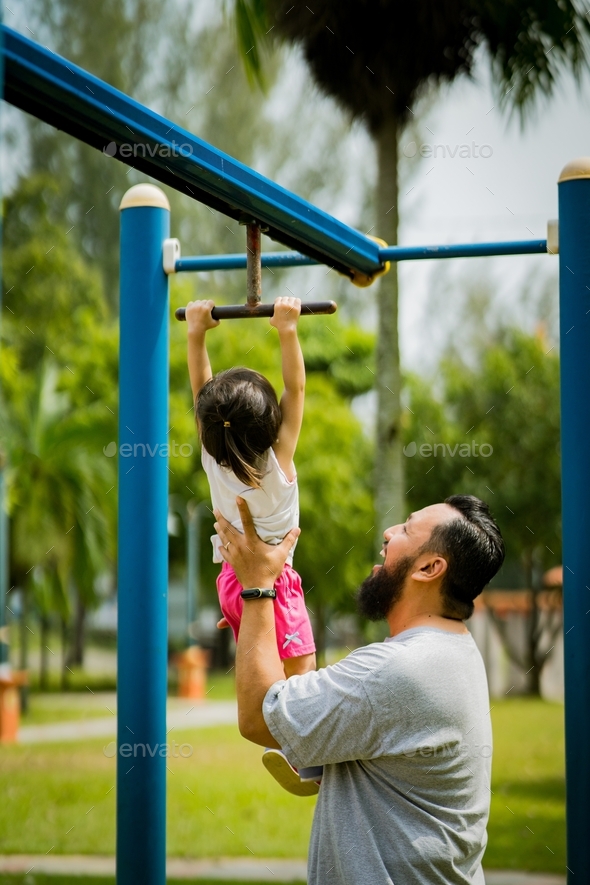 toddler hanging from the monkey bar while being held by the bearded father in the park