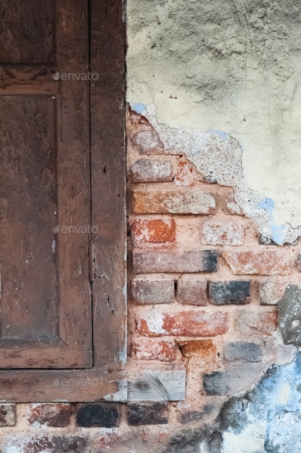 Worn out building, bare wall with red bricks next to the wooden window