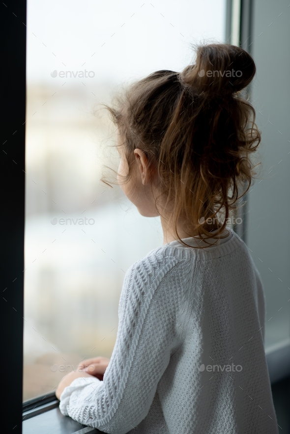 A cute little girl looks out the window. House. Comfort. Atmosphere.
