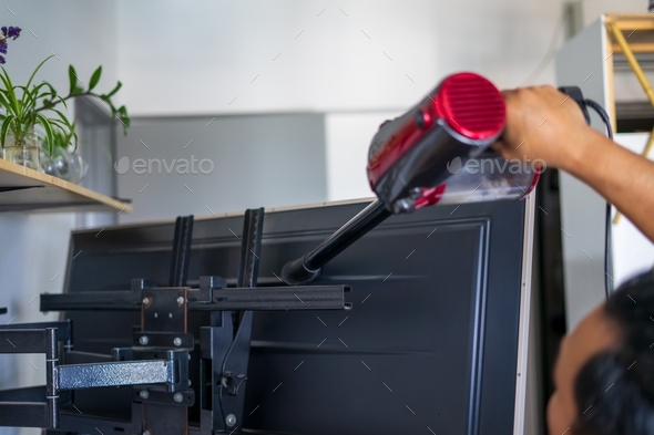 A man vacuum cleaning behind television At Home.