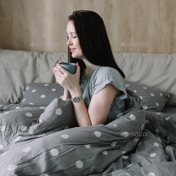 morning, coziness, cozy home concept - a young woman with cup of coffee or cacao in bed at home