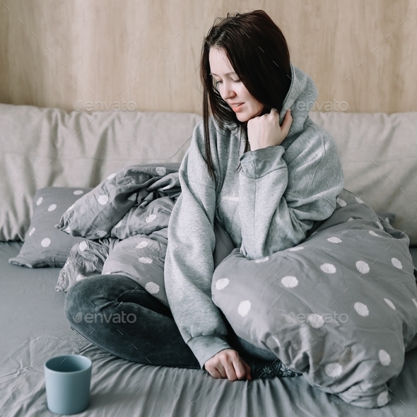 morning, coziness, cozy home concept - a young woman with cup of coffee or cacao in bed at home