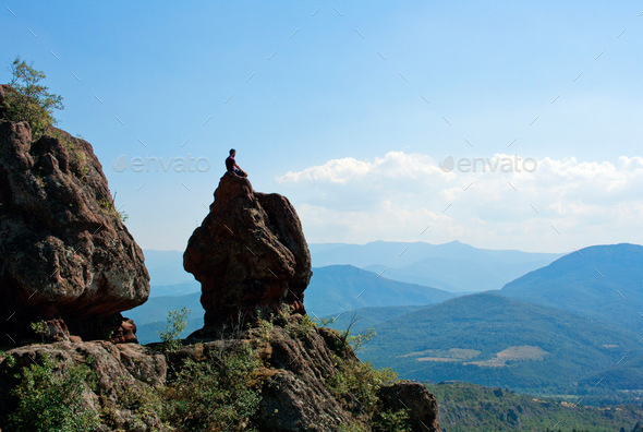 A guy meditating on the top of the rock after hiking to the summit of the mountain, mountains view