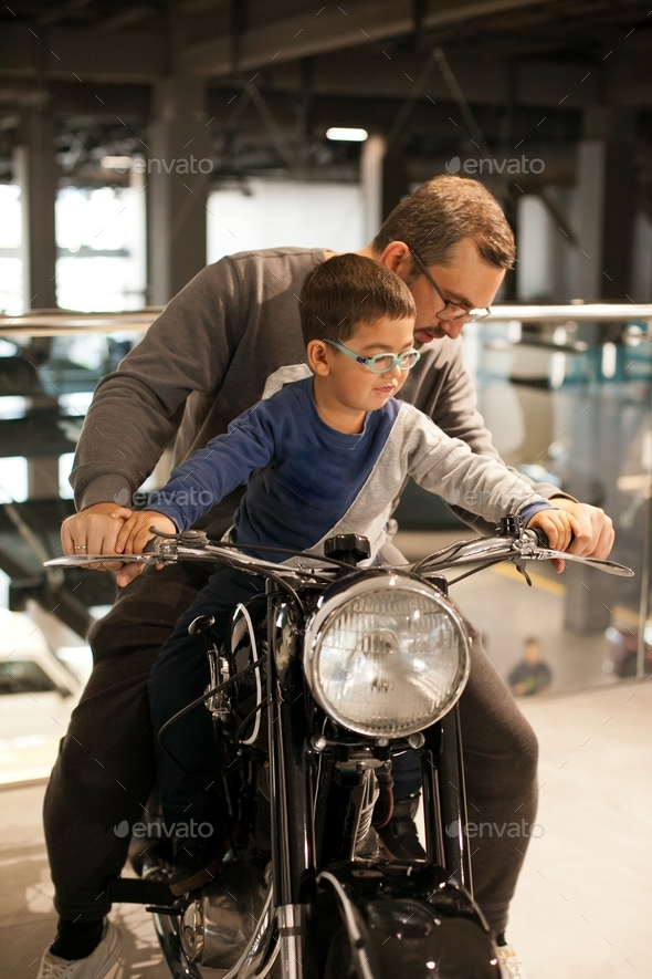 Father and son in glasses at a interactive car show or museum on a motorbike - fun family time