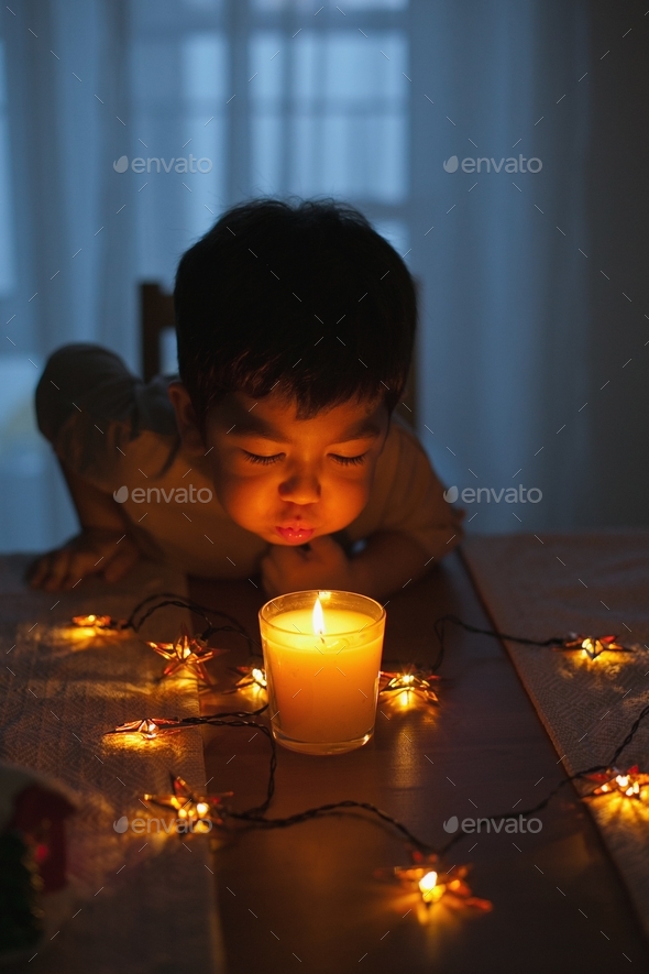 A cute little boy with candlelight blowing on a candle to make a wish