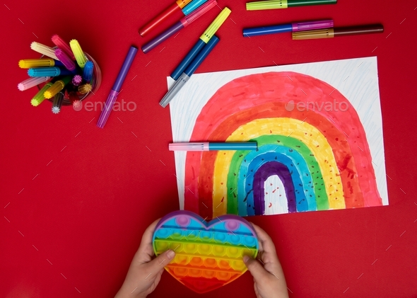 A cute girl in rainbow clothes draws a rainbow with multi-colored markers. House. Childhood.