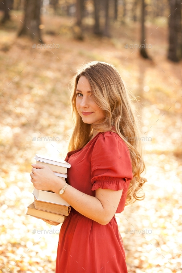 Beautiful woman holding a stack of books in the park, autumn colors, reading time, books aesthetic