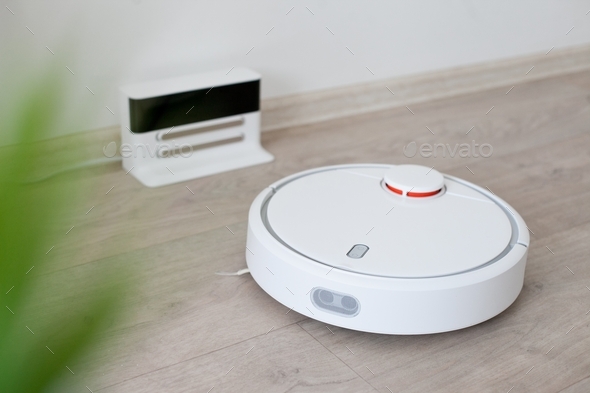 A white robot vacuum cleaner on the floor with a green house plant, everyday cleaning, dusting floor