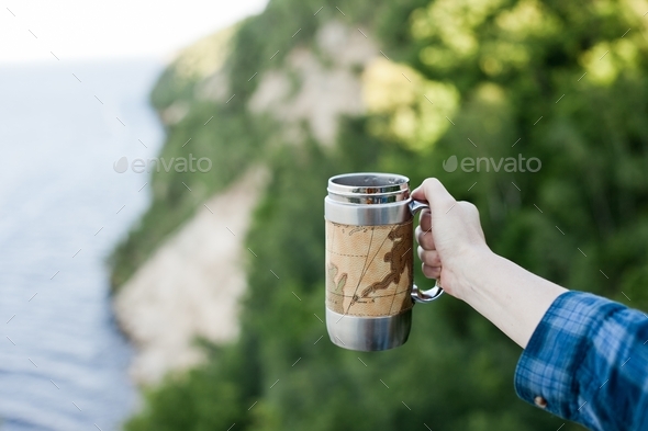 Young woman holding a travel mug on a rock at campsite, mug life, camping, adventure, hiking, summer