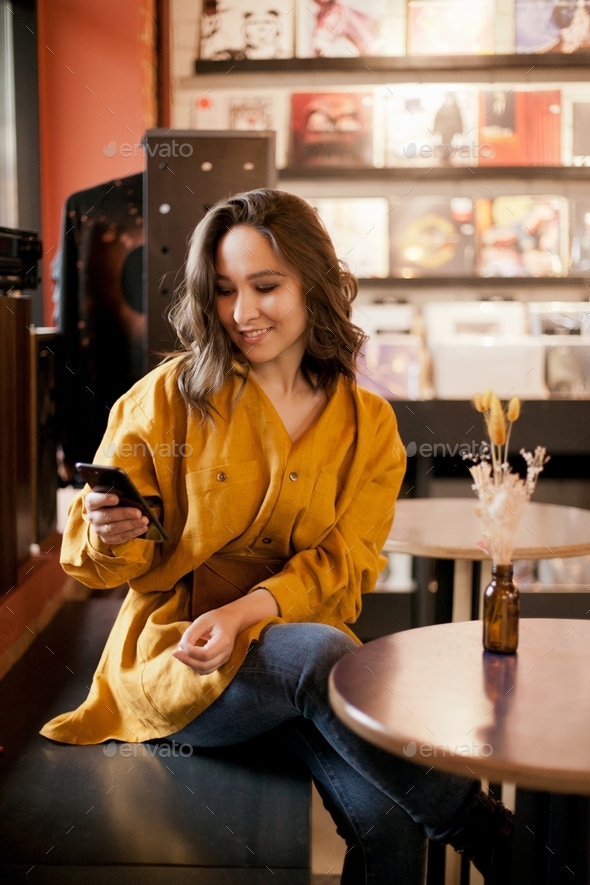 Woman using mobile, checking her social media at a table in a cafe, social life, holding a phone