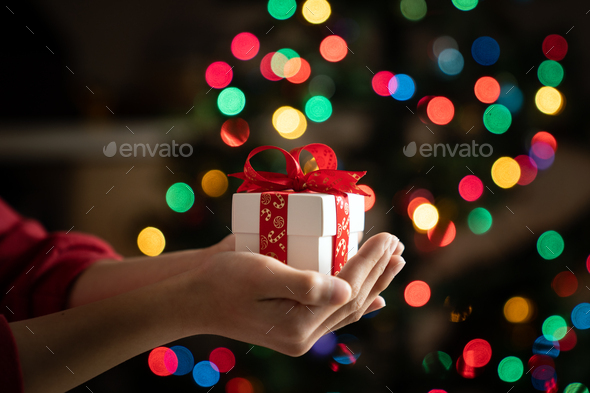 Hand holding gift in front of chirstmas tree - Stock Photo - Images