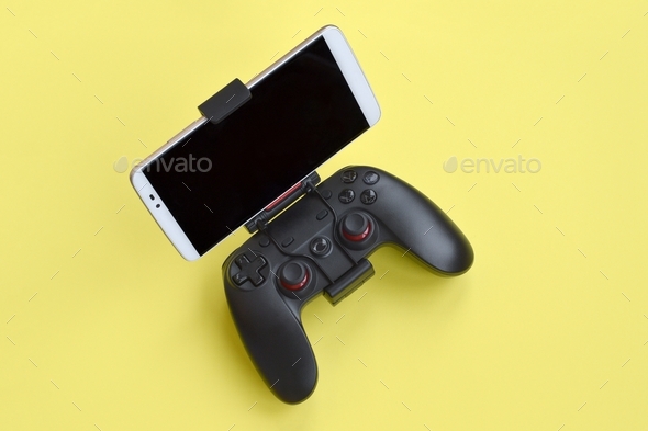 Modern black gamepad for smartphone on yellow background close up. Mobile video gaming device