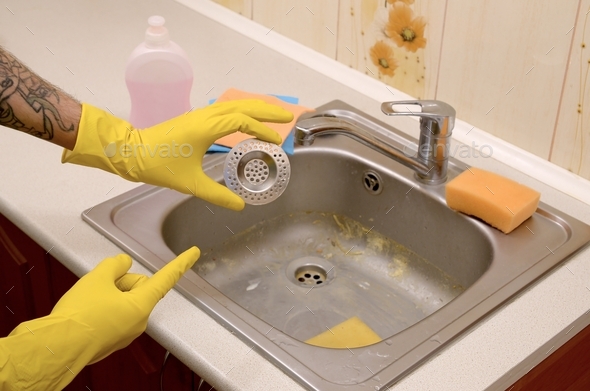 Cleaner in rubber gloves shows clean plughole protector of a kitchen sink