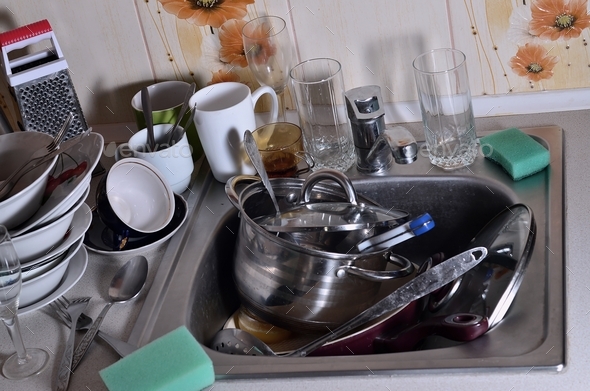 A huge pile of unwashed dishes in the kitchen sink and on the ...