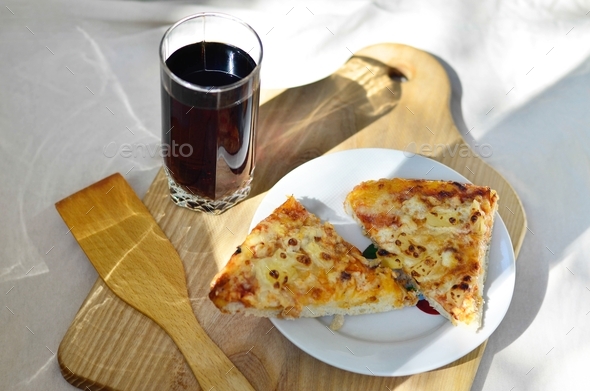 Pieces of pineapple pizza and glass cup of cola on wooden plate