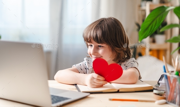 Smiling child boy with Valentine greeting card having a video call chat on laptop, online dating, en