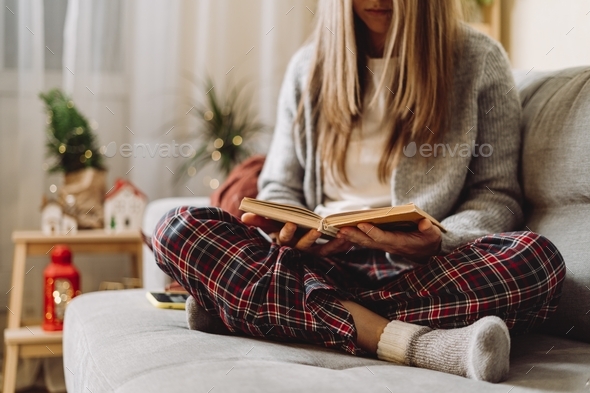 Cozy vibes. Woman relax at home on couch and reading book. Hygge winter Christmas decor