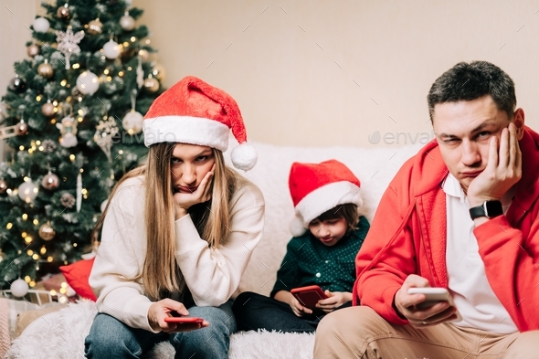 Portrait of depressed family with son playing cell phone during new year party. Tired mom and dad ha