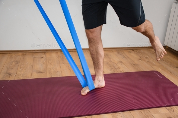 Lower section of man working out and exercising with stretching band on yoga mat.