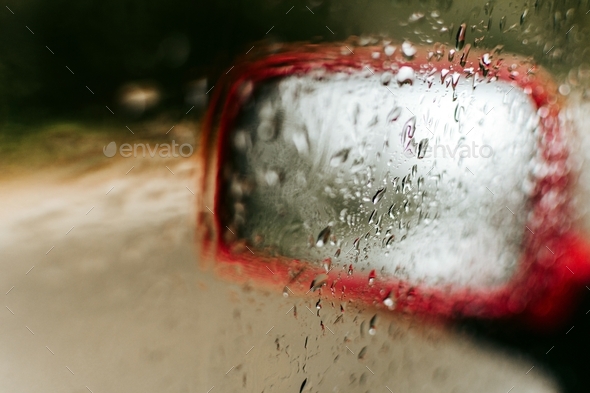 Foggy car window with rain drops. Side view mirror of a red car.