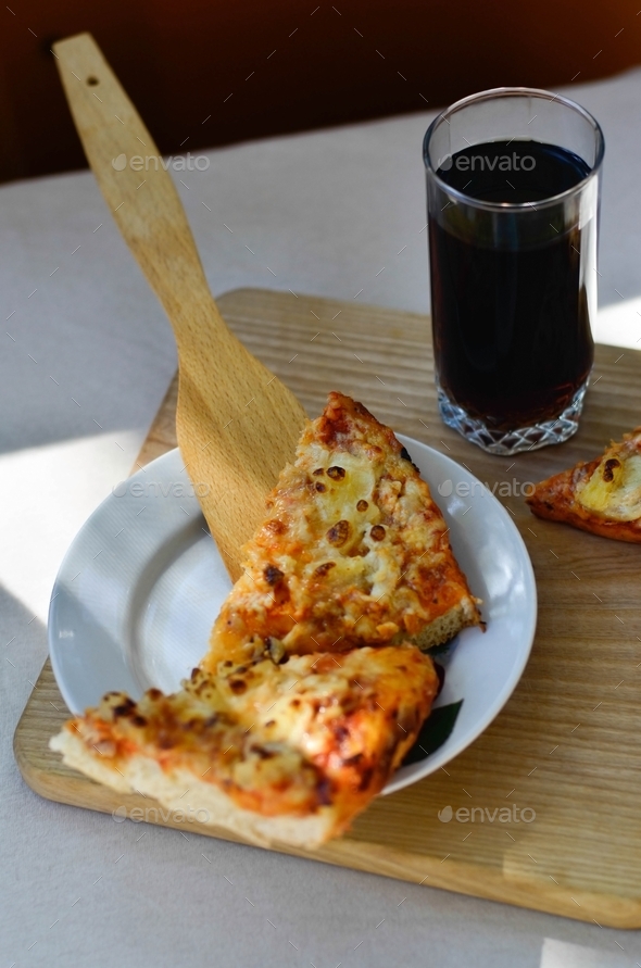 Pieces of pineapple pizza and glass cup of cola on wooden plate
