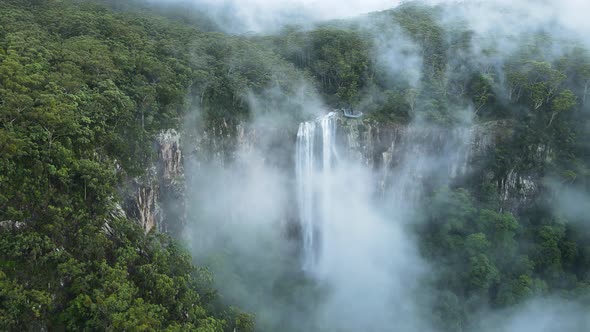 Unique view of a fog covered mountain revealing a majestic tropical waterfall lookout platform. Cine alt