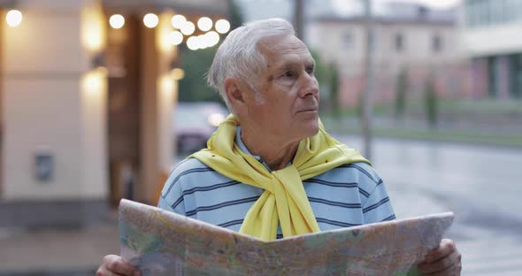 Senior Male Tourist Exploring Town with a Map in Hands and Looking for the Route alt