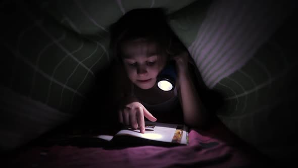 Little Child Girl Reading a Book with a Flashlight alt