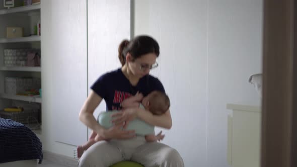 A Young Mother Rocks Her Baby on a Fitness Ball alt