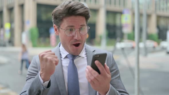 Middle Aged Businessman Celebrating on Smartphone, Outdoor alt