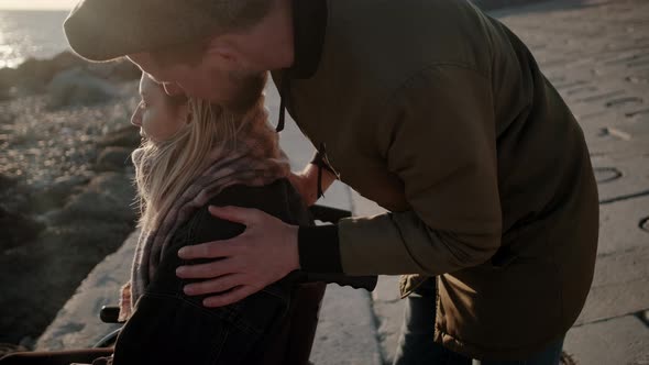 Man Is Stroking Head of His Beloved Woman in Wheelchair on Sea Coast alt