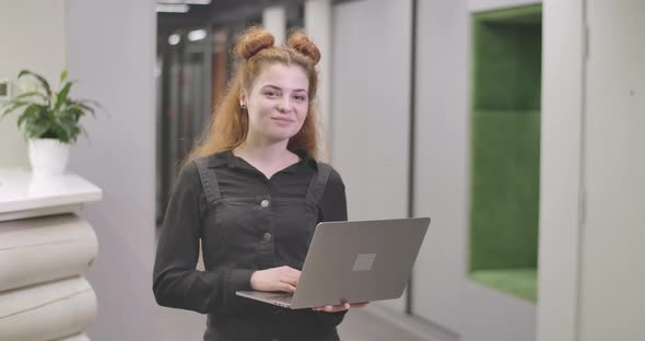 Portrait of Beautiful Redhead Caucasian Woman Standing with Laptop in Open Space Office alt