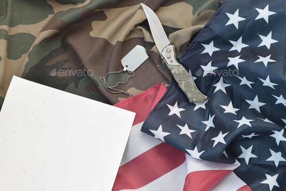 Blank paper lies with knife and army dog tag necklace on camoufl