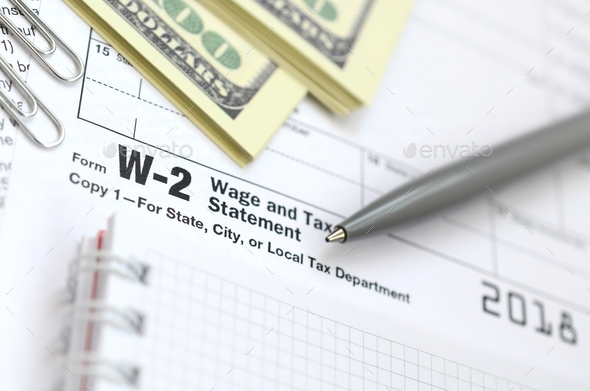 The pen, notebook and dollar bills is lies on the tax form W-2 Wage and Tax Statement