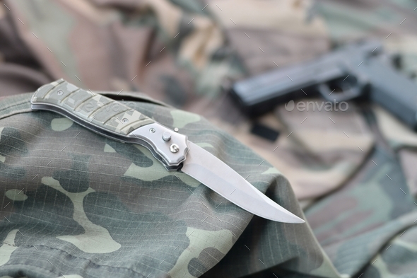 Tactical knife and pistol lie on camouflage green fabric