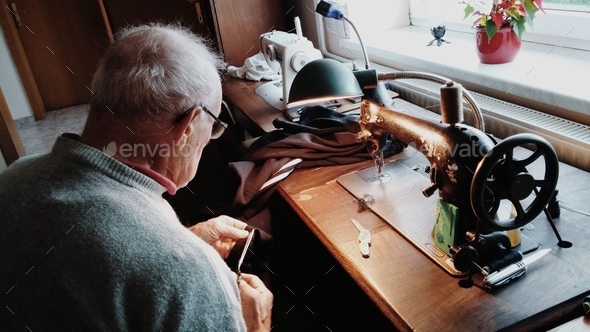Old tailor working behind a sewing machine.