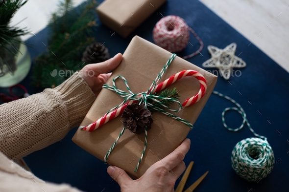 woman wraps a handmade eco style christmas present in kraft paper and natural spruce branches