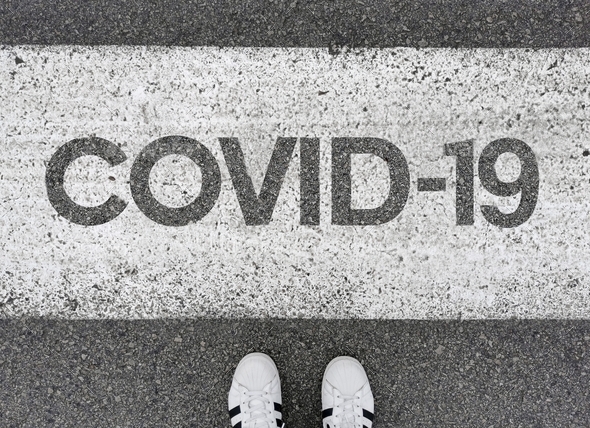 Personal perspective of person looking down at Covid-19 text painted on road.