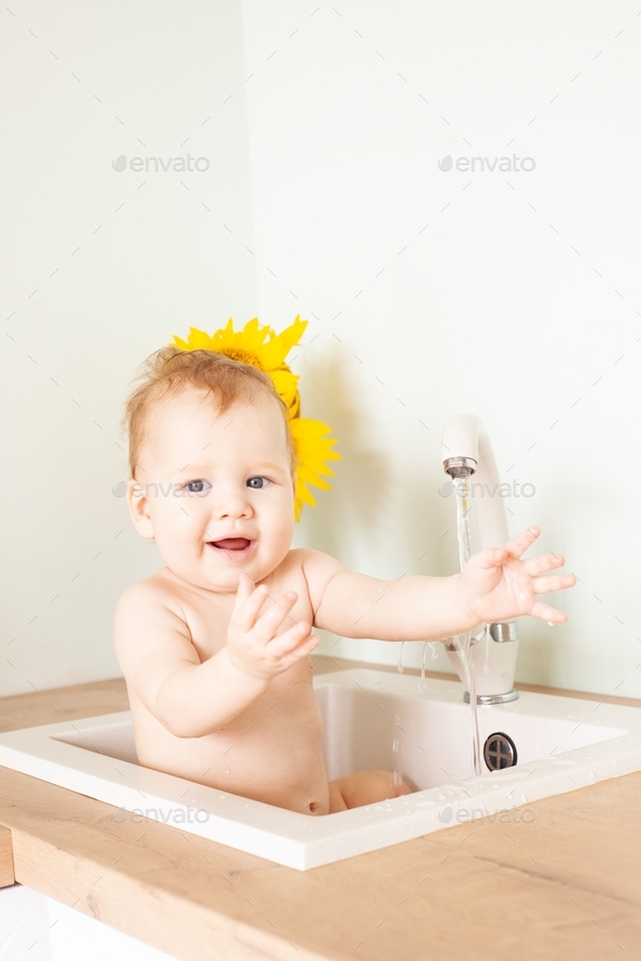 Baby taking bath in kitchen sink. Little boy bathing. Water fun for