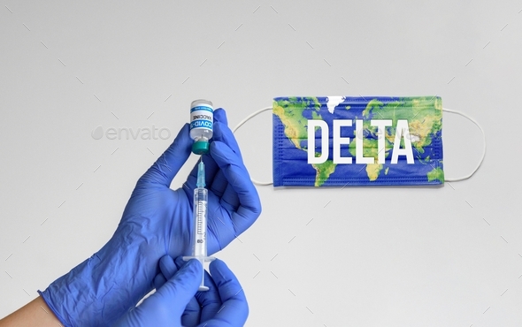 Close-up of doctor holding syringe and vaccine vial. Face mask in background.